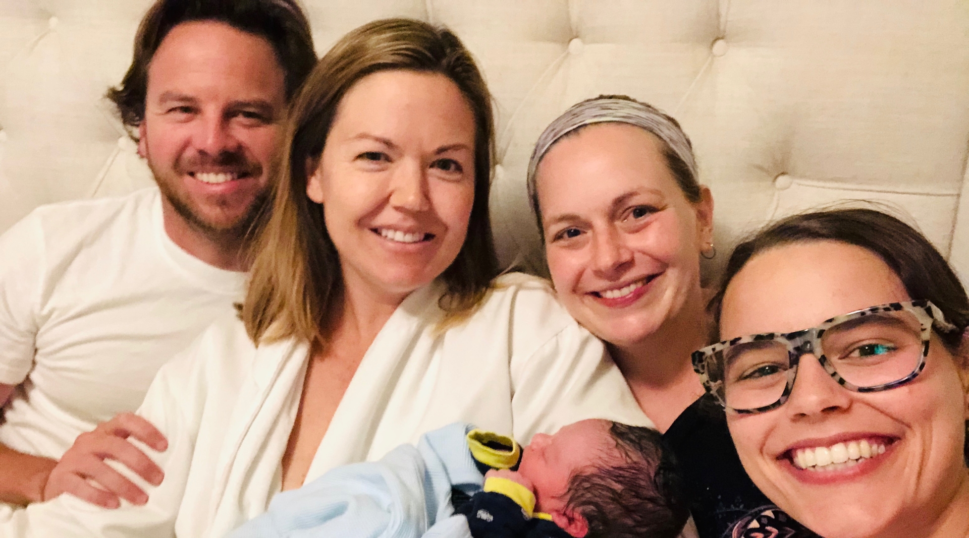 A mother holding her newborn, sits beside her partner, midwife, and doula.