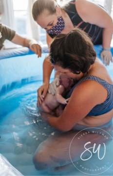 A mother holds her new baby in a birth tub.