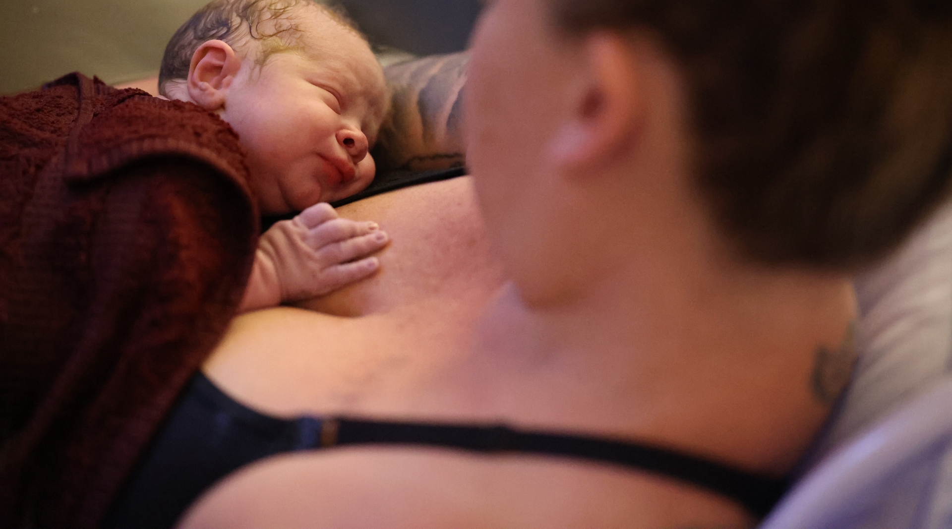 A mother looks down at her sleeping newborn baby.