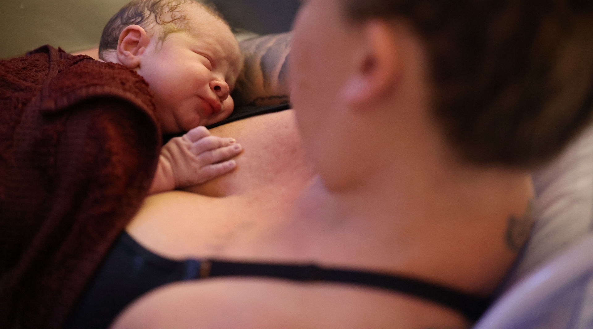 A mother looks down at her sleeping newborn baby.